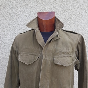 Puede incluir: Una chaqueta de trabajo verde con cierre de botones y dos bolsillos grandes. La chaqueta está hecha de un material duradero, similar a la lona.