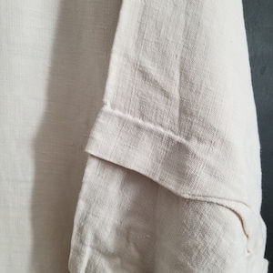 May include: A close-up of a white linen fabric with a textured weave. The fabric is folded over itself, creating a layered effect.