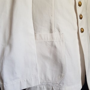 May include: White linen jacket with a single patch pocket on the left side and gold buttons on the right side.