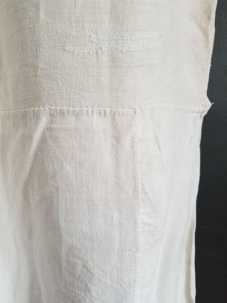 May include: A white linen fabric with a subtle texture. The fabric has a seam running horizontally across the middle.