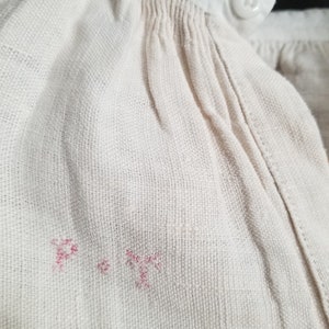 May include: Close-up of a white fabric with a pink embroidered "P" and a pink embroidered "T" on the fabric.