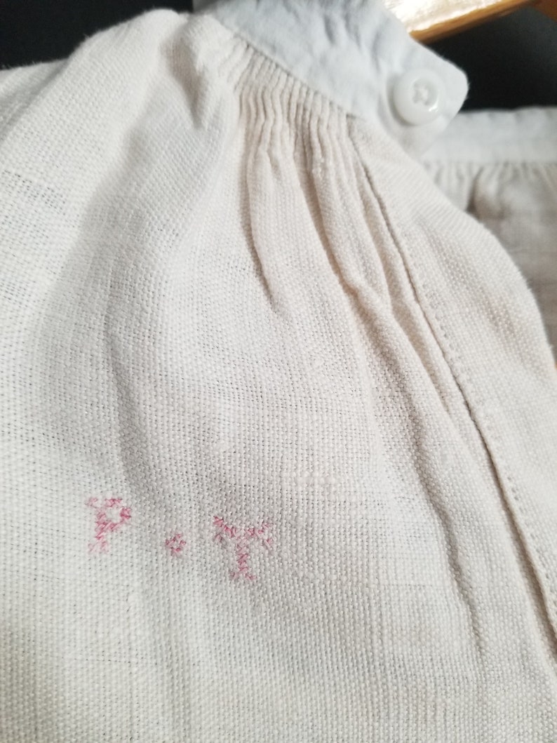 May include: Close-up of a white fabric with a pink embroidered "P" and a pink embroidered "T" on the fabric.
