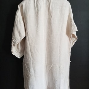 May include: A white linen tunic shirt with a button-up collar and three-quarter sleeves. The shirt has a relaxed fit and a slightly longer length.