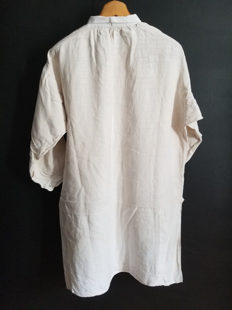 May include: A white linen tunic shirt with a button-up collar and three-quarter sleeves. The shirt has a relaxed fit and a slightly longer length.