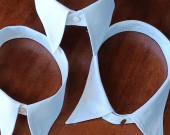 May include: Three white detachable shirt collars with button closures are displayed against a brown background. The collars vary in style, including rounded and pointed designs, offering versatile options for formal wear.