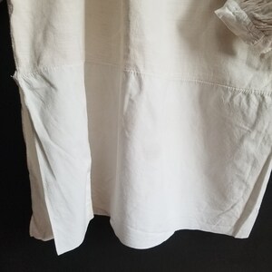 May include: A white linen shirt with a gathered sleeve detail. The shirt has a simple design and is made of a lightweight fabric.
