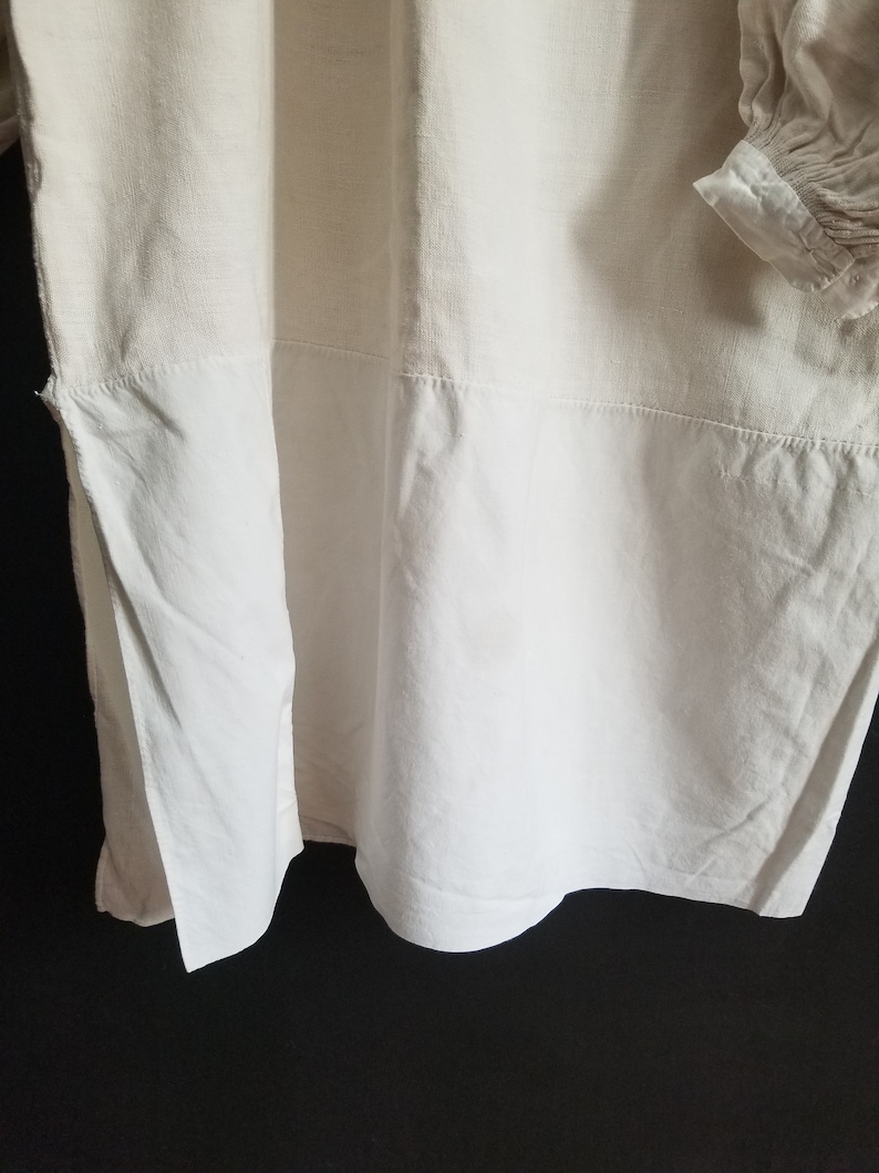 May include: A white linen shirt with a gathered sleeve detail. The shirt has a simple design and is made of a lightweight fabric.