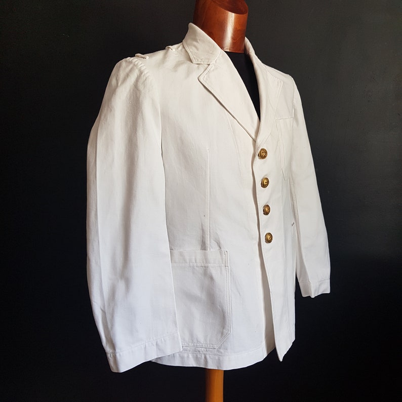 May include: A white blazer with a single-breasted closure and gold buttons. The blazer has a pocket on the left side and a notched collar.