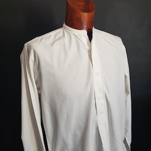 Peut inclure: Une chemise blanche à manches longues avec un col mandarin et une fermeture boutonnée à l'avant. La chemise a une coupe ample et est faite d'un tissu léger.