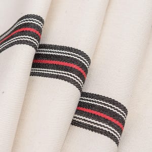 Może przedstawiać: Biały materiał w czarne i czerwone paski. Materiał jest złożony i pokazuje paski biegnące poziomo wzdłuż materiału.