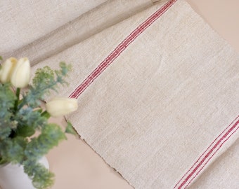 May include: A white linen table runner with red stripes. The runner is rolled up at one end, and there are flowers in a vase in the foreground.