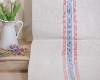May include: A white linen tea towel with red and blue stripes. The towel is folded in half and has a herringbone pattern.