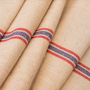 May include: Cream-colored fabric with a herringbone weave and red and blue stripes. The fabric is folded in thirds, showing the stripes on each fold.