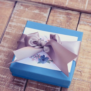 A blue gift box tied with a silver satin ribbon, accompanied by a white card featuring a floral design packaging example.