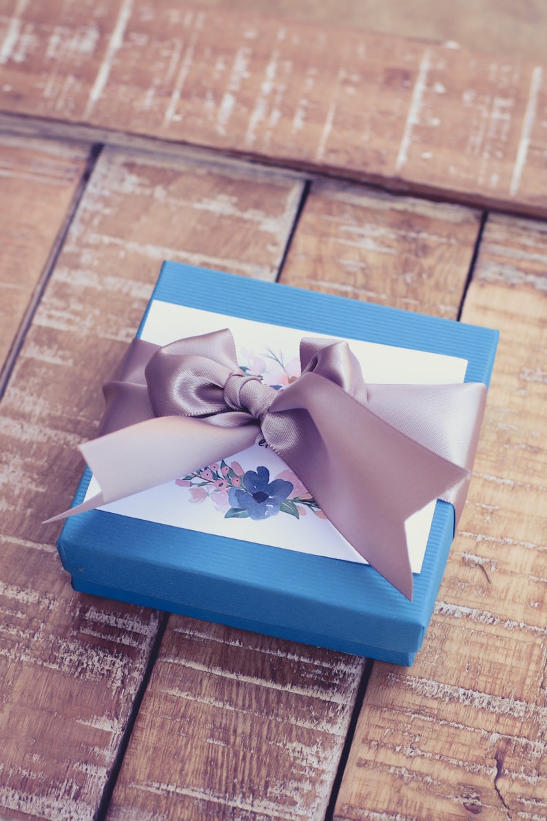 A blue gift box tied with a silver satin ribbon, accompanied by a white card featuring a floral design packaging example.