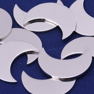 May include: A group of silver crescent moon charms, arranged on a blue fabric background.