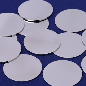 May include: A group of ten silver-colored round metal discs on a blue background.