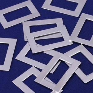 Könnte beinhalten: Eine Gruppe von rechteckigen Metallrahmen in Silberfarbe mit abgerundeten Ecken. Die Rahmen sind in einem zufälligen Muster auf einer blauen Oberfläche angeordnet.