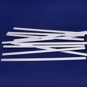 May include: A pile of silver-colored metal strips on a blue background. The strips are flat and rectangular, and they are arranged in a random pattern.