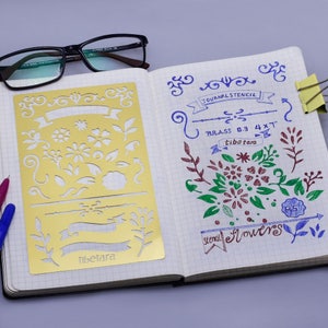 May include: A gold metal stencil with floral and banner designs. The stencil is labelled "JOURNAL STENCIL" and "tibetara". The stencil is 0.3 mm thick and 4 x 7 inches.