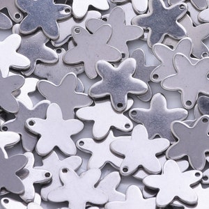 May include: A close-up of a pile of silver metal flower charms. The charms are all the same size and shape, and they have a small loop at the top for attaching to jewelry.