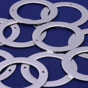 Op de afbeelding: Een groep zilveren metalen ringen, sommige met kleine gaatjes, op een blauwe achtergrond.