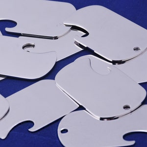 Könnte beinhalten: Eine Gruppe von silbernen Flaschenöffnern aus Metall mit abgerundeter rechteckiger Form. Die Flaschenöffner haben eine glatte, glänzende Oberfläche und ein kleines Loch oben.
