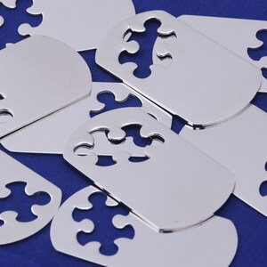 Könnte beinhalten: Eine Gruppe von silbernen Metall-Puzzleteilen mit einem Ausschnittmuster. Die Teile sind auf einem blauen Hintergrund angeordnet.