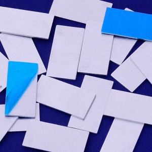 May include: A collection of rectangular silver metal sheets, some with a blue adhesive backing, on a blue background.
