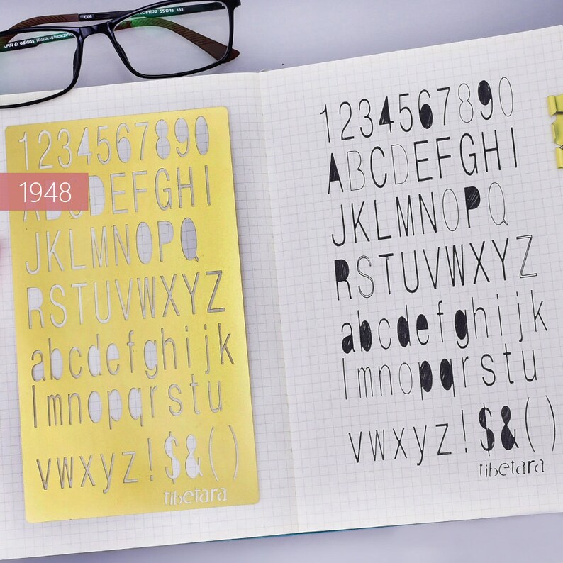May include: A yellow plastic stencil with the numbers 1 through 9 and the letters of the alphabet in uppercase and lowercase. The stencil is on a notebook page with the same letters and numbers written in pencil.