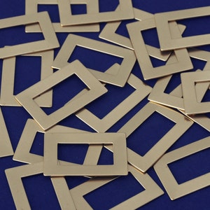 Könnte beinhalten: Ein Stapel goldfarbener Metallrahmen auf blauem Hintergrund. Die Rahmen sind rechteckig und haben eine glatte, polierte Oberfläche.