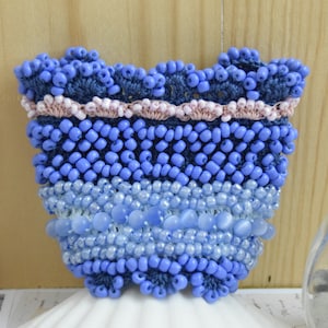 May include: A blue and pink beaded bracelet with a crocheted design. The bracelet is made with a variety of blue beads, including small round beads, larger oval beads, and iridescent beads.