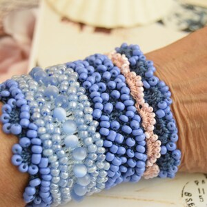 May include: A blue and pink beaded bracelet with a crocheted design. The bracelet is made with different sizes and shapes of beads.