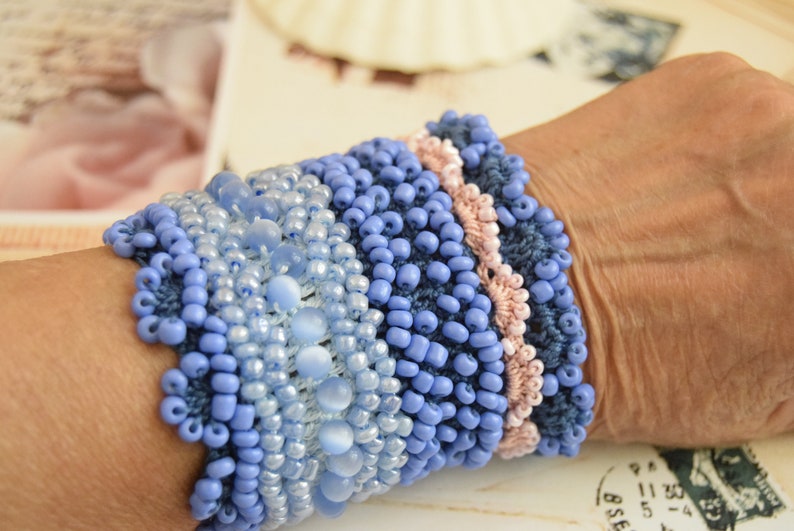 May include: A blue and pink beaded bracelet with a crocheted design. The bracelet is made with different sizes and shapes of beads.