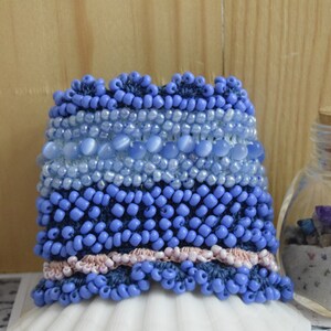 May include: A blue beaded bracelet with a pink and blue trim. The bracelet is made of different sizes and shapes of blue beads, including some larger, oval-shaped beads.