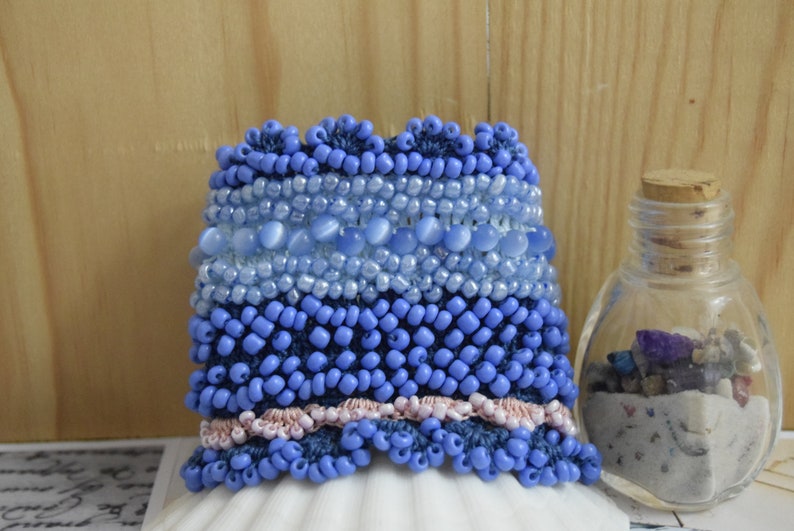 May include: A blue beaded bracelet with a pink and blue trim. The bracelet is made of different sizes and shapes of blue beads, including some larger, oval-shaped beads.