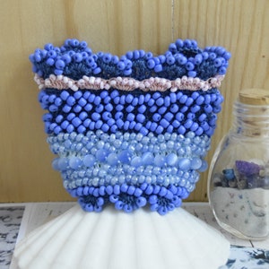 May include: A blue and white beaded purse with a pink trim. The purse is sitting on a white seashell.