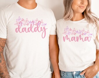 May include: A couple wearing white t-shirts with pink floral designs and the words "daddy" and "mama" printed on them. They are holding hands.