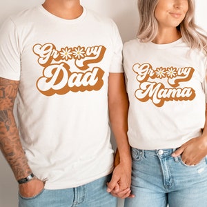 May include: Two white t-shirts with a retro font design. The text on the shirts reads "Groovy Dad" and "Groovy Mama".