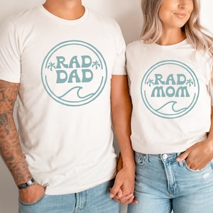 May include: A couple wearing white t-shirts with a blue circle design. The man's shirt says "RAD DAD" and the woman's shirt says "RAD MOM".