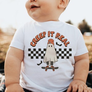 May include: White baby t-shirt with a ghost wearing a red hat and skateboarding. The text "CREEP IT REAL" is in an orange arch above the ghost.