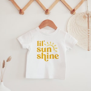 May include: White baby onesie with a yellow graphic that says "Lil' sun shine" with a stylized sun graphic.