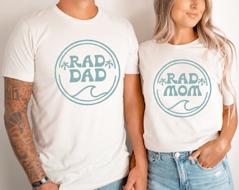 May include: A couple wearing white t-shirts with a blue circle design. The man's shirt says "RAD DAD" and the woman's shirt says "RAD MOM".