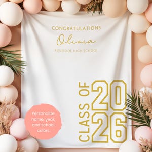 May include: A white graduation banner with gold text and a pink circle for personalization. The banner reads "Congratulations Olivia Riverside High School" and "Class of 2026". The banner is surrounded by pink, white, and beige balloons.