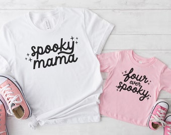 May include: Two white t-shirts with black text. The larger shirt says "spooky mama" and the smaller shirt says "four ever spooky".