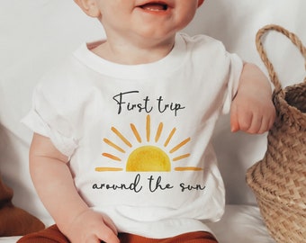 Peut inclure: Un body blanc pour bébé avec un soleil jaune et le texte "First trip around the sun".