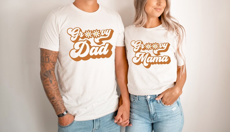 May include: Two white t-shirts with a retro font design. The text on the shirts reads "Groovy Dad" and "Groovy Mama".