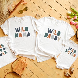 May include: Four white t-shirts with colorful text. The shirts say "Wild Mama", "Wild Daddy", "Born Two Be Wild", and "Wild Sister".