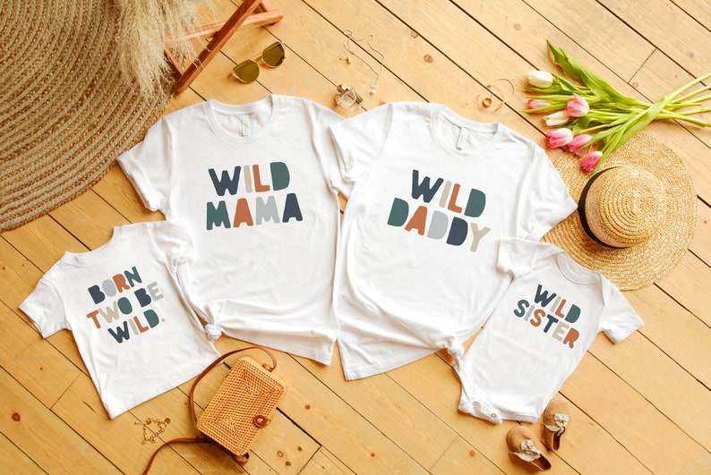 May include: Four white t-shirts with colorful text. The shirts say "Wild Mama", "Wild Daddy", "Born Two Be Wild", and "Wild Sister".