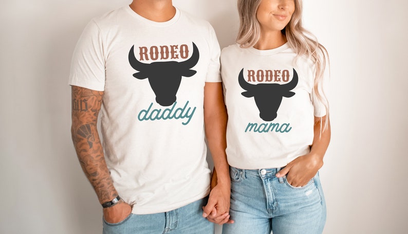 May include: A couple wearing white t-shirts with a black bull silhouette and the text "RODEO daddy" and "RODEO mama" in brown and blue.